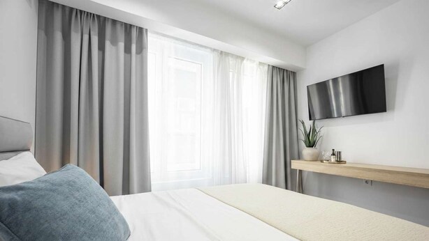 Een moderne hotelkamer met een bed, gordijnen, een wandtelevisie en een kamerplant.