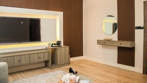 A modern hotel room with a large flat-screen TV, a wooden console table, a mirror, and a built-in shelf. - Ambiiflora Hotel (Abuja)