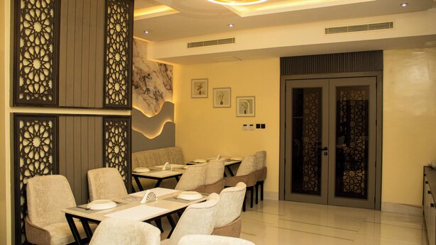 A modern dining area with tables and chairs, decorative panels, and a marble wall. - Ambiiflora Hotel (Abuja)
