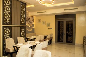 A modern dining area with tables and chairs, decorative panels, and a marble wall. - Ambiiflora Hotel (Abuja)
