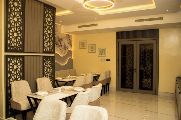 A modern dining area with tables and chairs, decorative panels, and a marble wall. - Ambiiflora Hotel (Abuja)