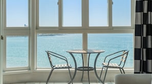 Une pièce dotée d’une grande fenêtre donnant sur la mer, d’une table ronde entourée de chaises et d’un rideau à rayures noires et blanches.