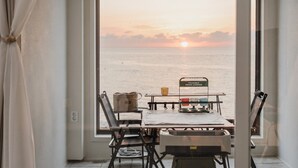 A room with a view of the sea at sunset, a table with a drink carrier, and a chair.