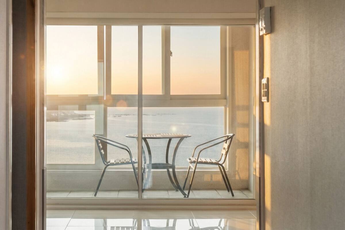 Un balcón con dos sillas y una mesa, con vista a un cuerpo de agua y una costa lejana.