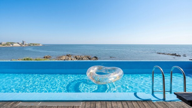 A pool with clear blue water, a heart-shaped inflatable float, and a view of the sea and distant buildings.