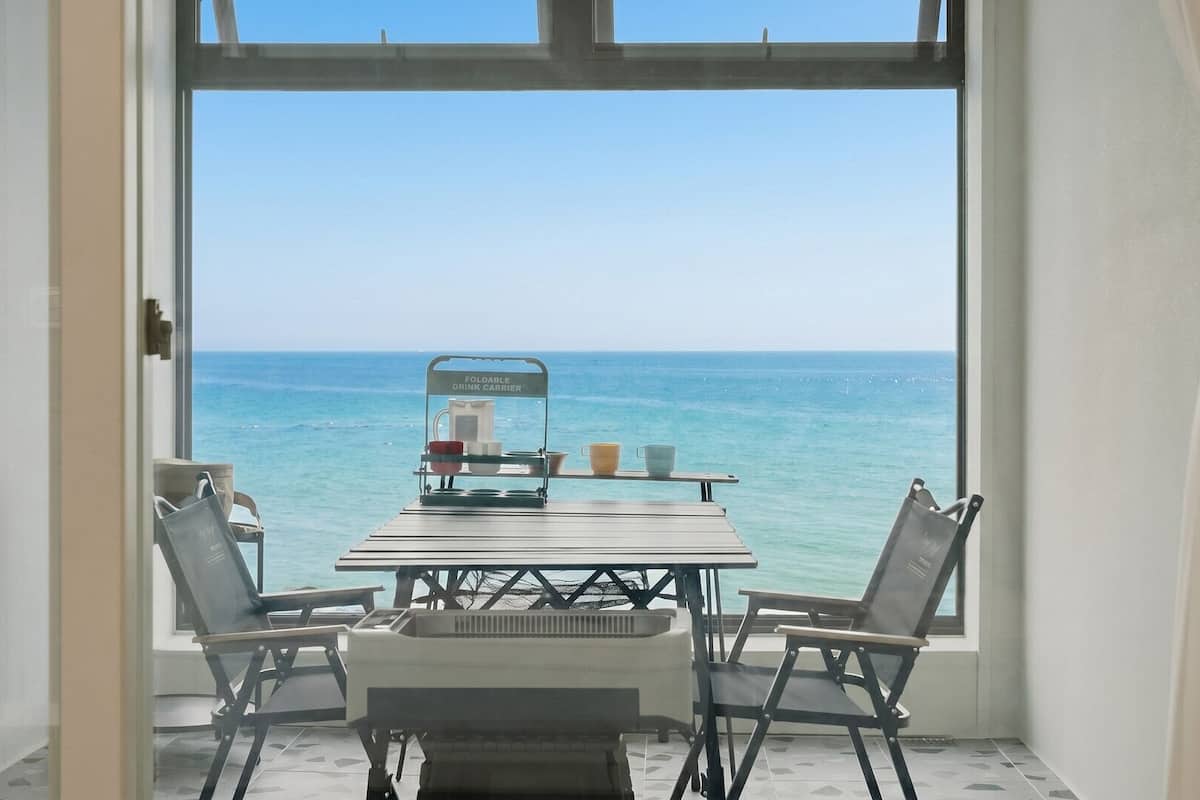 Una habitación con una mesa y sillas frente a un ventanal con vista al mar.