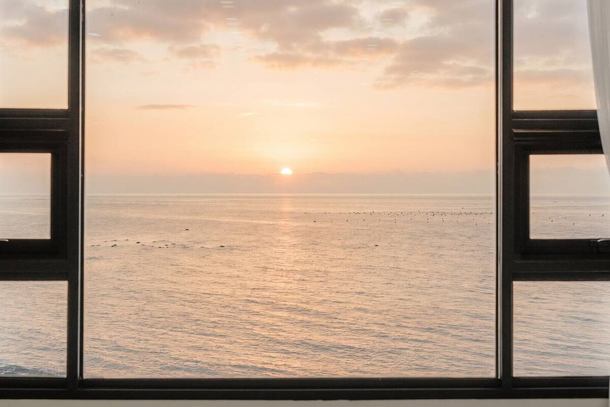 Una ventana con vista al océano al atardecer.