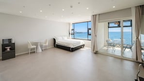 Une chambre moderne avec un lit, une table à manger, des chaises, un téléviseur et une vue sur la mer.