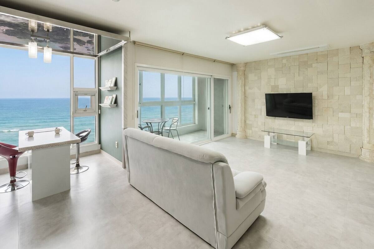 Un moderno salón con un amplio ventanal con vistas al océano, un televisor de pantalla plana en la pared y un diseño minimalista.