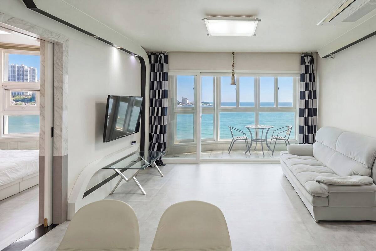 Una habitación de hotel moderna con sofá, televisor, mesa de comedor, sillas y vista al mar.