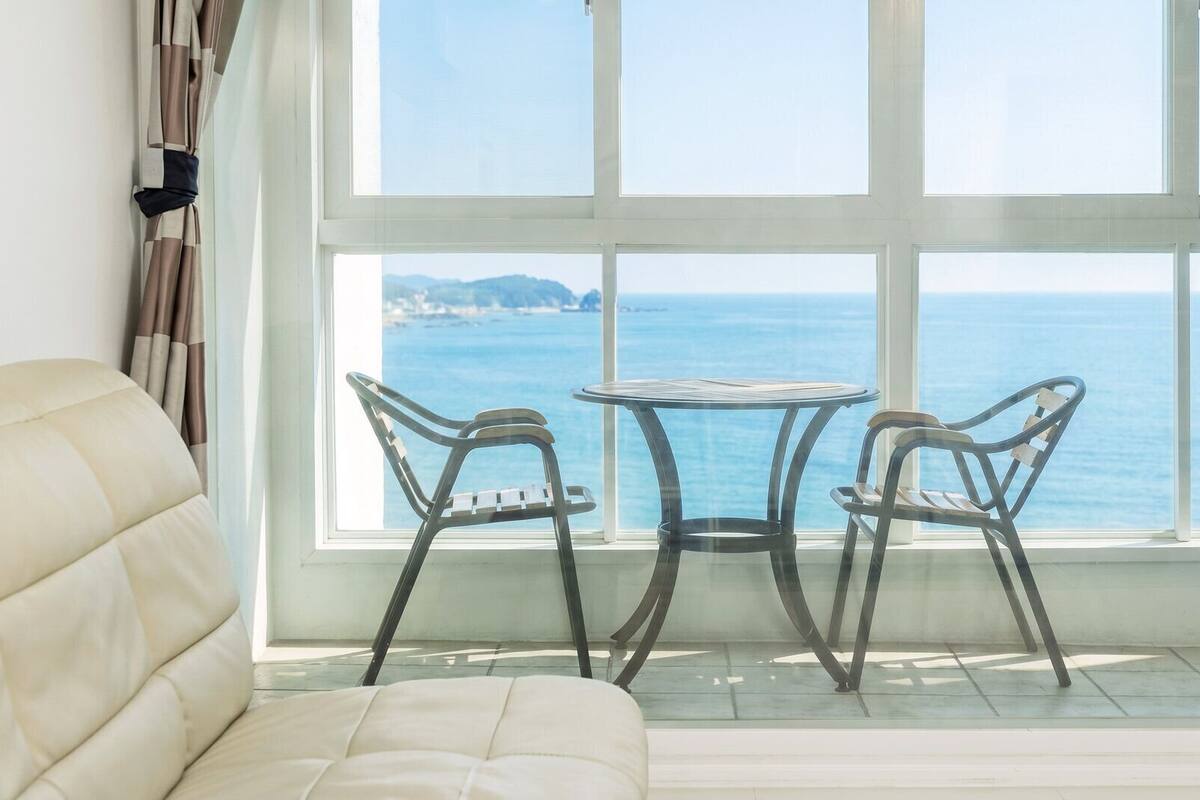 Una habitación con un ventanal grande, un sofá acolchado y dos sillas de metal.