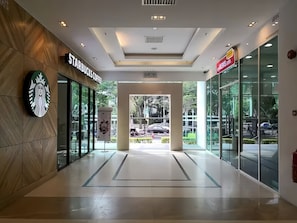 Una entrada moderna de edificio con un letrero de Starbucks Coffee, un letrero de KEW GARDEN y otro letrero de KEW GARDEN a la derecha.