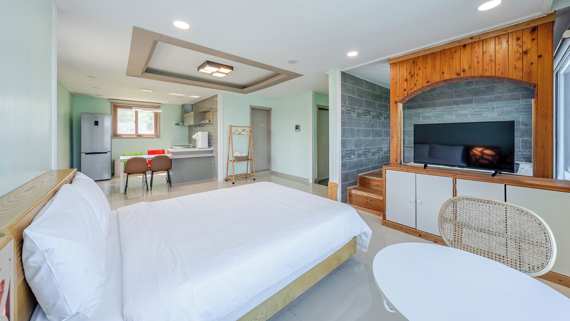 A hotel room with a bed, a small kitchenette, a TV, and a dining area.