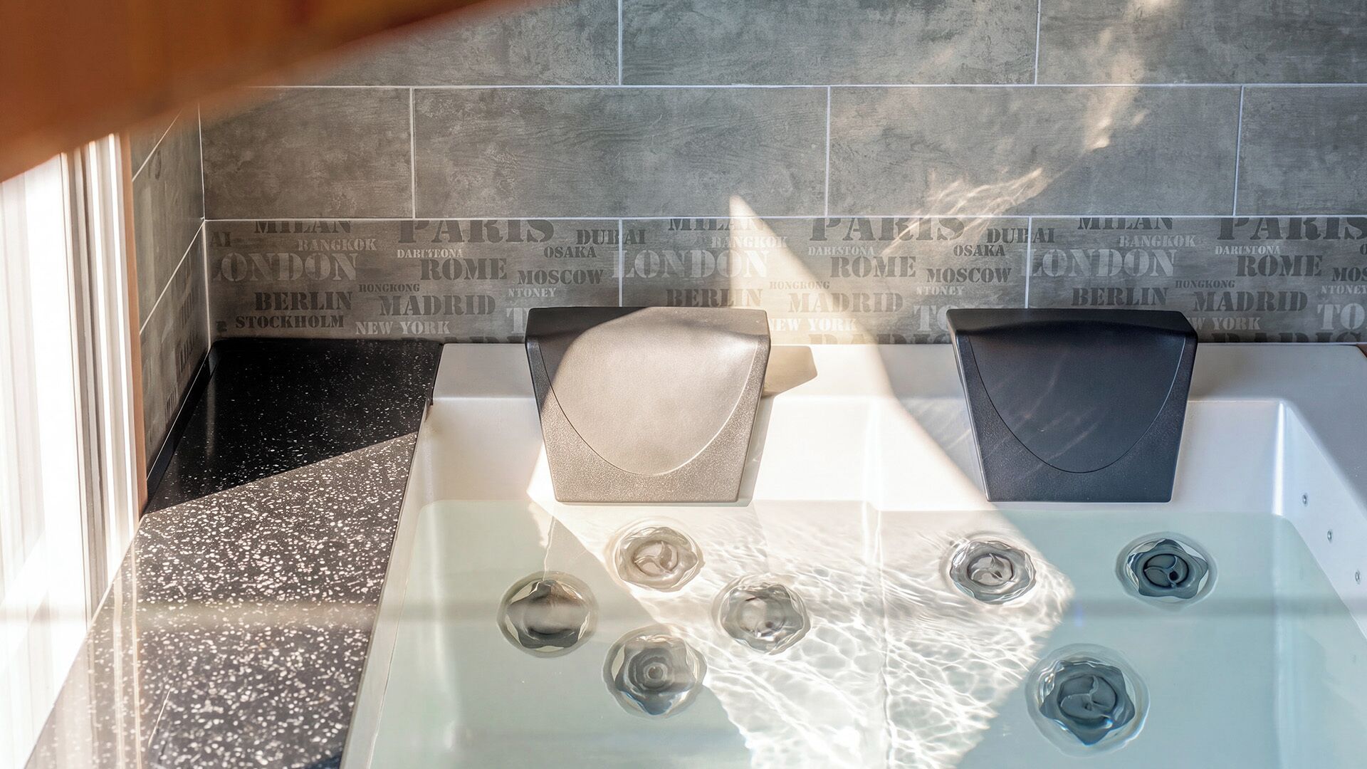 Une salle de bain avec un mur recouvert de carreaux sur lequel figurent des noms de villes, une baignoire et un espace douche.