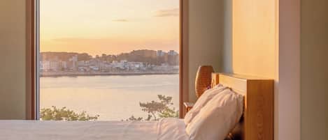Ein Bett mit Holzvorhang, Blick auf eine Stadtlandschaft über dem Wasser, und ein Fenster mit Sonnenuntergangsblick.