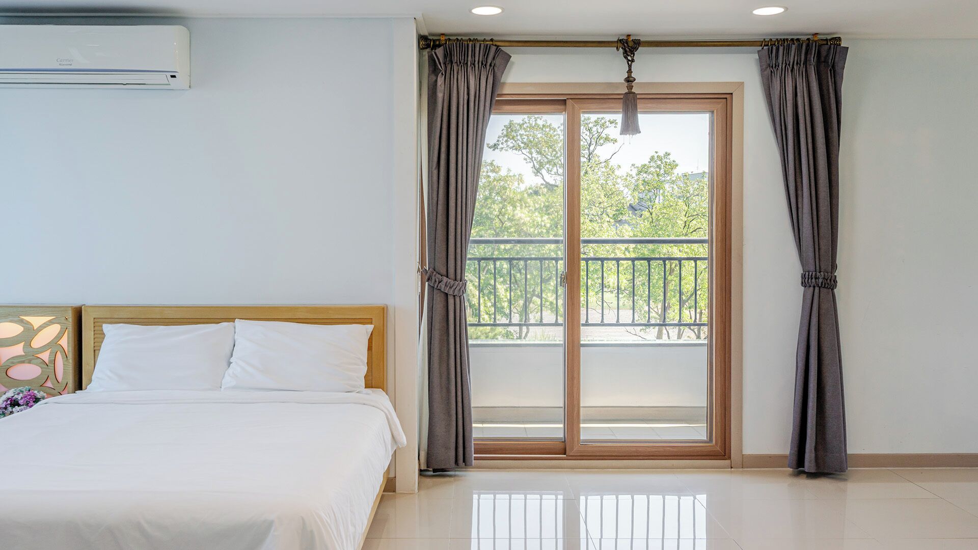 A hotel room with a bed, a balcony with a railing, and a view of trees.