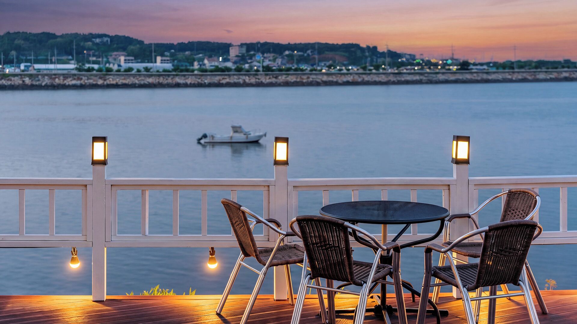 A deck with wicker chairs and a table, overlooking a calm body of water with a boat in the distance.