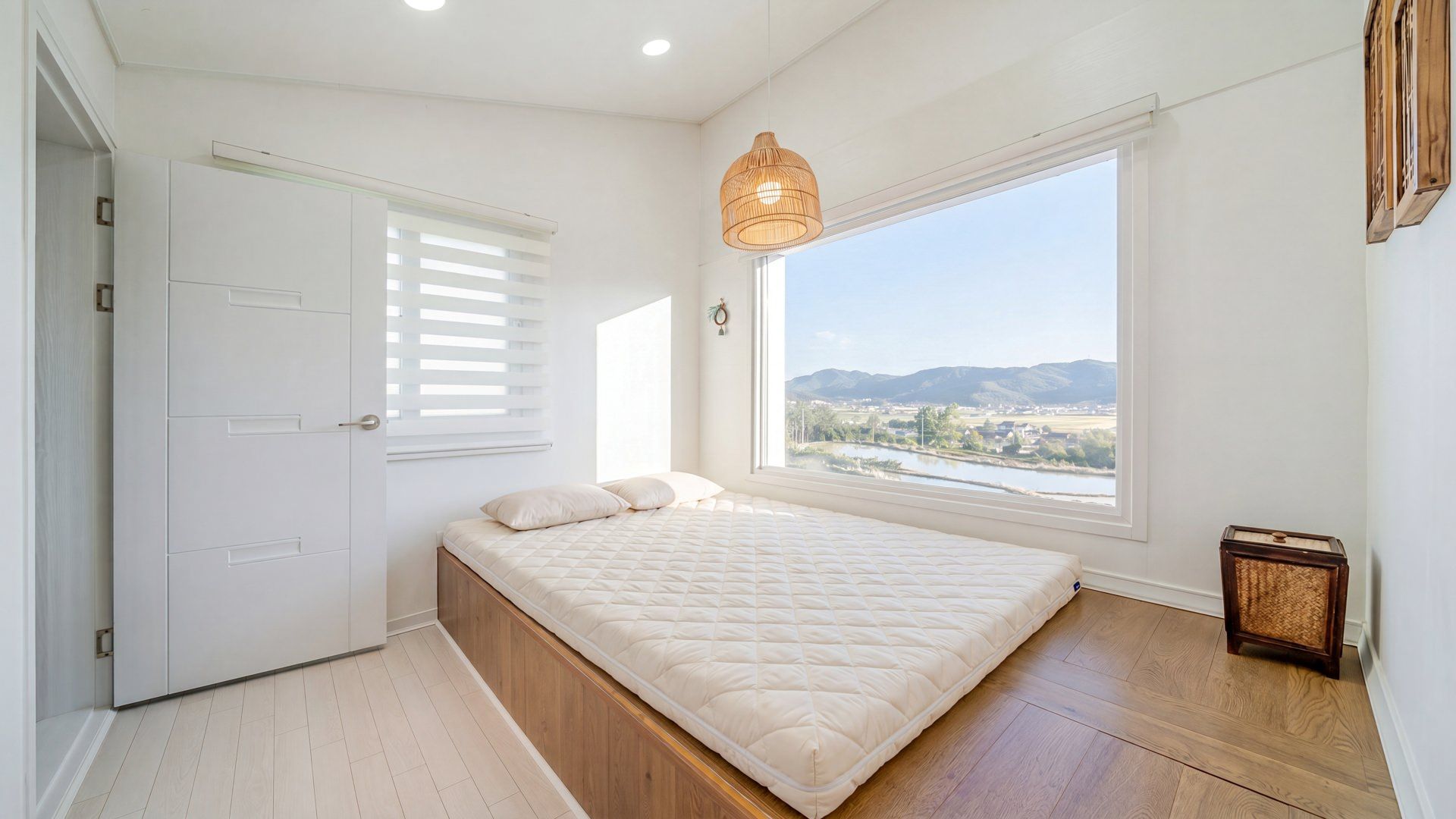 A bedroom with a bed, a window with a view, a door, and a small wooden table.