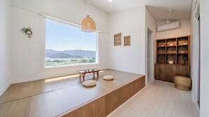 A room with a large window, a wooden bench, a hanging light fixture, and a built-in wooden shelf with items. - Gyeongju The Glamping Pool Villa (Gyeongju)