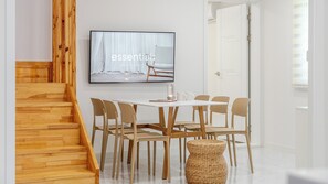 Een modern interieur met een houten trap, een eettafel met stoelen, een aan de muur bevestigde televisie en een witte deur.