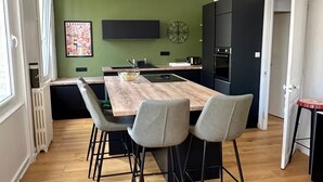 A modern kitchen with a wooden island, two grey chairs, a black refrigerator, and a green accent wall. - Le Triplex Grand Appart Vue Théâtre  (Cherbourg-en-Cotentin)