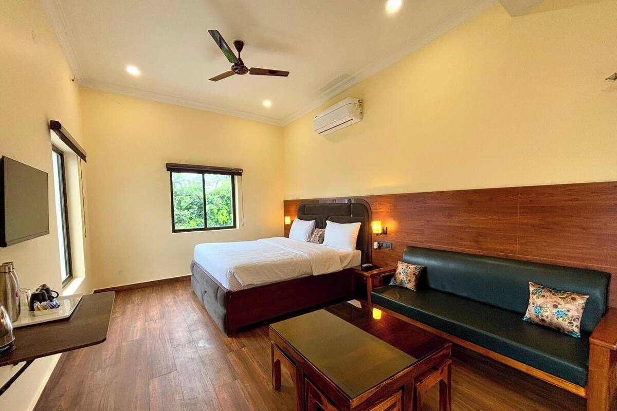 Una habitación de hotel con una cama, un sofá verde, una mesa de centro de madera, un ventilador de techo y un equipo de aire acondicionado.