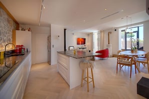 A modern kitchen with a central island, a dining area with wooden chairs, and a large window providing natural light. - Villa Pont Saint-Victor with Private Pool, 4 Bedrooms (Cannes)