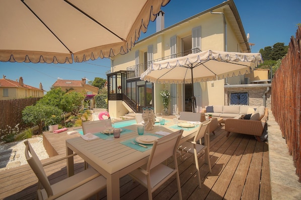 A wooden deck with a table set for dining, outdoor furniture, and a covered area with a view of a house. - Villa Pont Saint-Victor with Private Pool, 4 Bedrooms (Cannes)