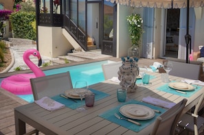 A poolside dining area with a table set for two, a pink flamingo float, and a staircase leading to a covered area. - Villa Pont Saint-Victor with Private Pool, 4 Bedrooms (Cannes)