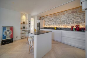 A modern kitchen with a central island, white cabinetry, a stone backsplash, and a minimalist design. - Villa Pont Saint-Victor with Private Pool, 4 Bedrooms (Cannes)