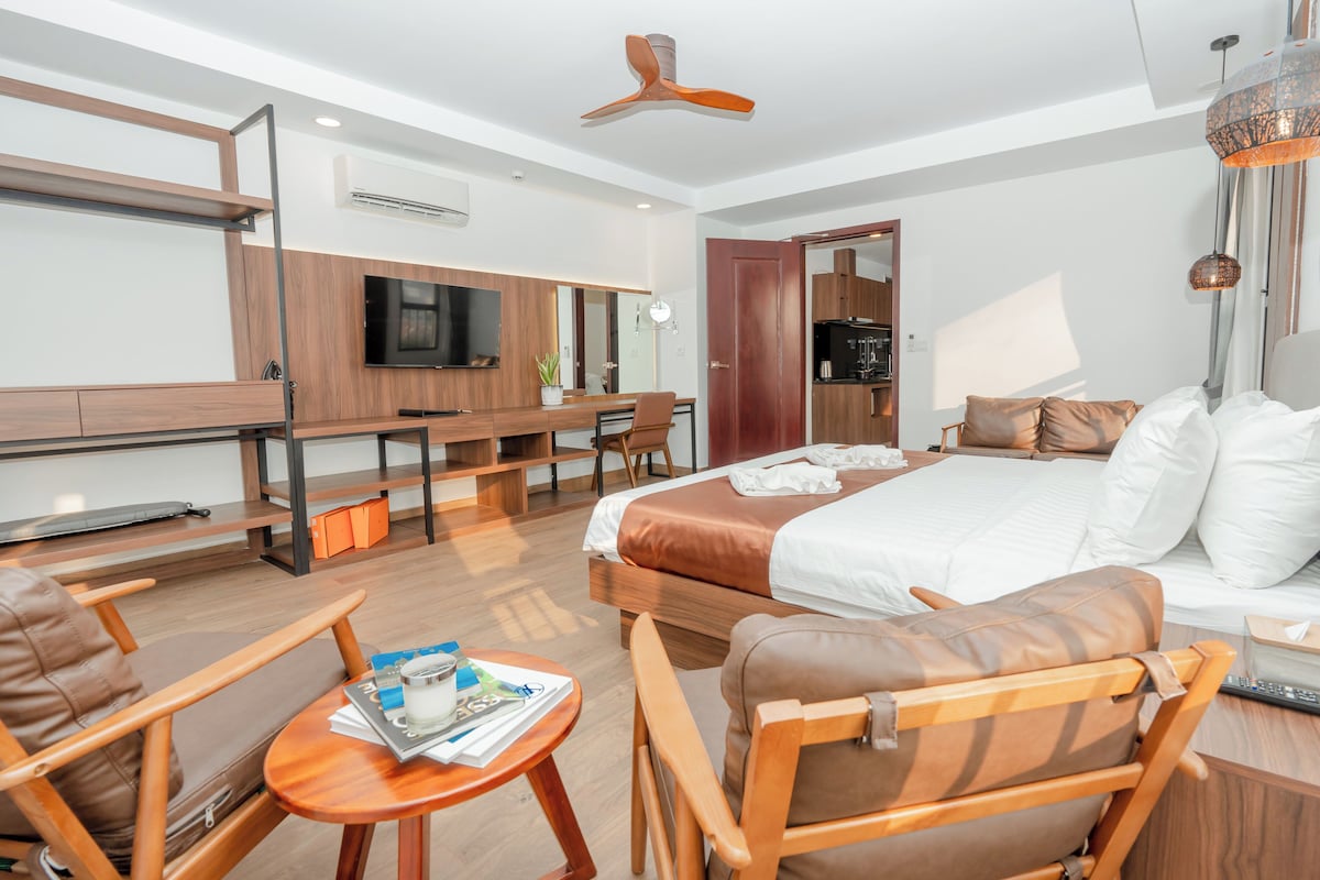 A hotel room with a bed, seating area, desk, television, and a kitchenette.