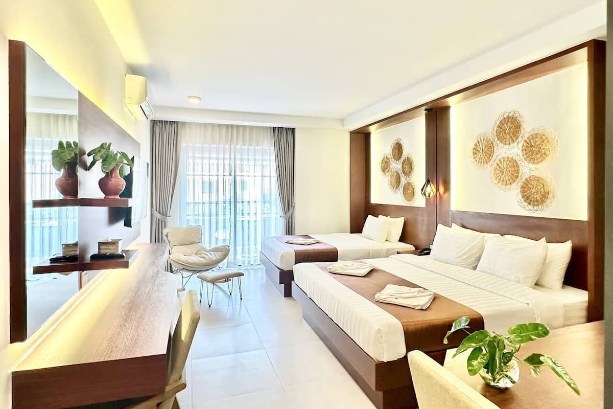 Habitación de hotel con una cama grande, un escritorio, una silla y una mesa de comedor. Hay dos plantas en macetas, una ventana con cortinas y una obra de arte en la pared.