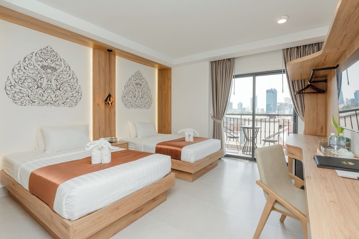 Habitación de hotel con dos camas, un escritorio y un balcón con vista a la ciudad.