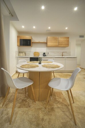 A modern kitchen with wooden cabinets, a round dining table with white chairs, and a marble countertop. - TOWNHOUSE 3 Bedroom Deluxe Apartment (Cannes)