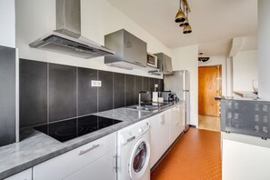Eine moderne Küche mit Einbauherd, Mikrowelle und Backofen, weißen Schränken und einer Waschmaschine.