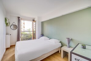 Ein Schlafzimmer mit Bett, Nachttisch, kleiner Topfpflanze, Spiegel und Blick ins Freie durch ein Fenster.