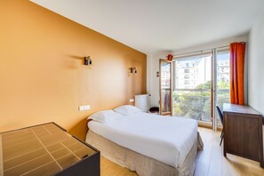 Ein Schlafzimmer mit Bett, Schreibtisch, Heizkörper und einem Fenster mit Vorhängen.