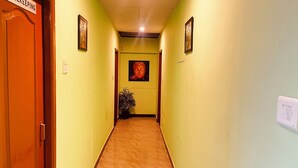 A hallway with a wooden door on the left, a potted plant in the center, and a Buddha statue on the wall. - Hotel Star City (Tiruchirappalli)