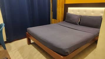 A single bed with a wooden frame and a headboard, a blue curtain, and a blue chair.