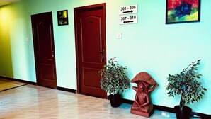 A hallway with two wooden doors, a Buddha statue, and potted plants. - Hotel Star City (Tiruchirappalli)
