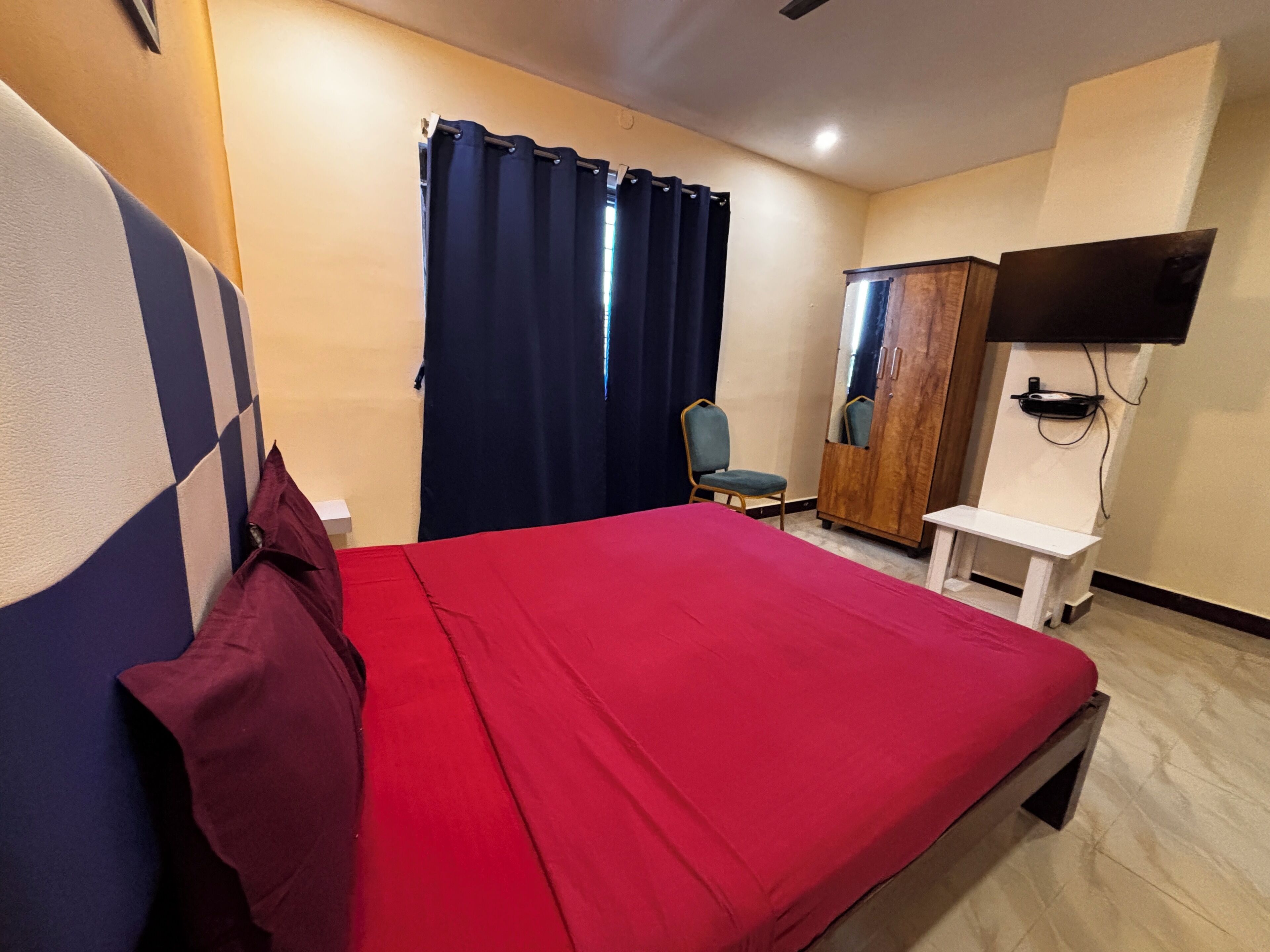 Quarto de hotel com cama, cadeira, guarda-roupa e televisão.