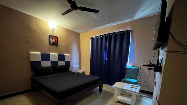 A bedroom with a bed, a desk, a chair, a ceiling fan, a TV, and a window with curtains. - Hotel Star City (Tiruchirappalli)