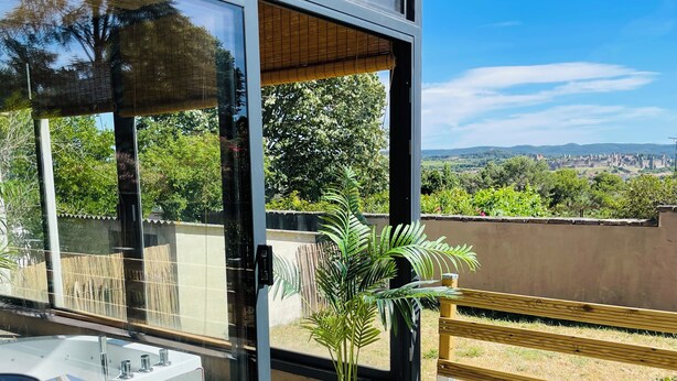 Un balcón moderno con puerta de cristal, una planta en maceta y vistas a un paisaje lejano.