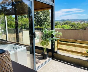 Ein moderner Balkon mit Glastür, einem Blumentopf und Blick auf eine entfernte Landschaft.
