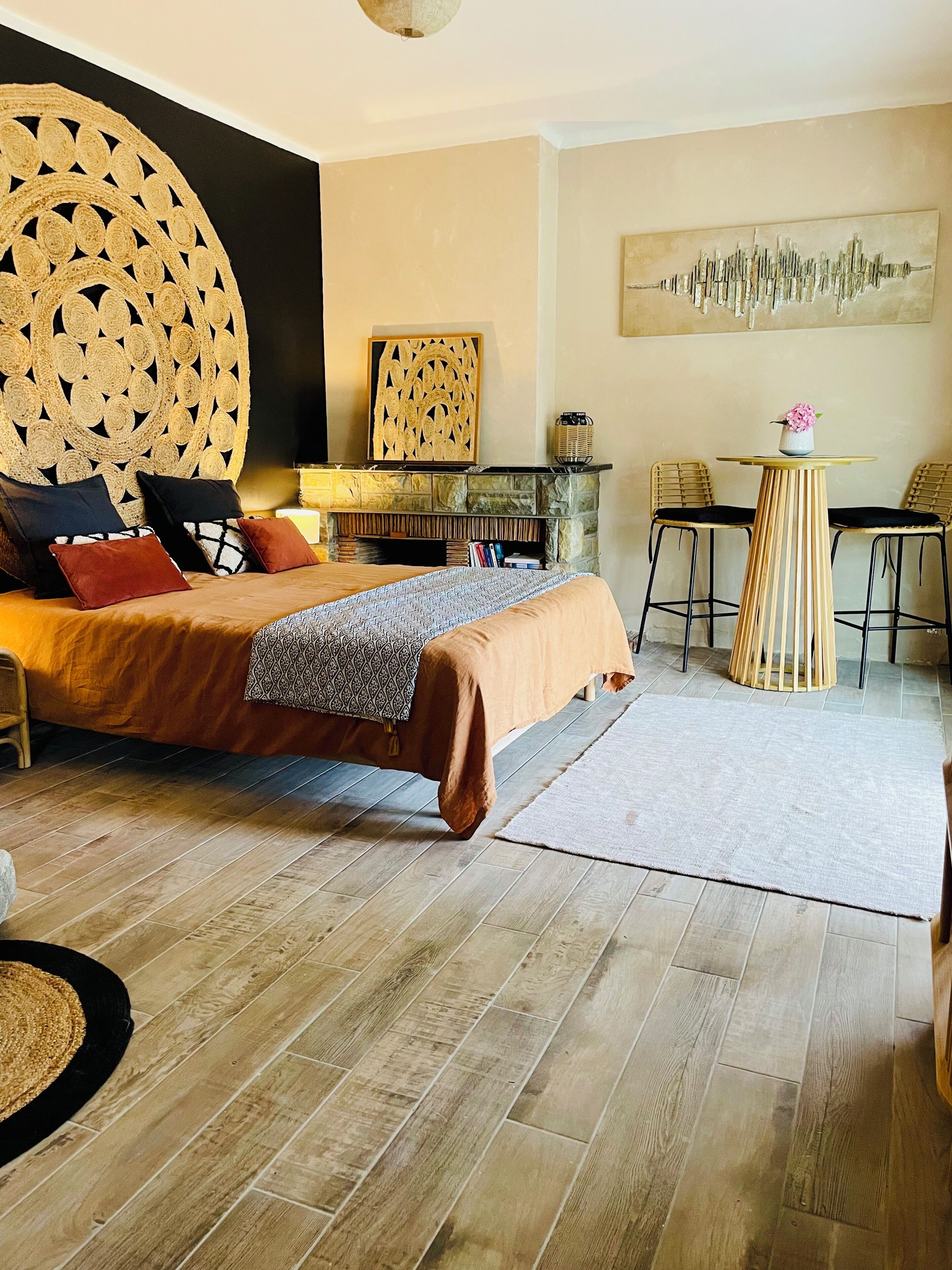 Un dormitorio con una cama grande, una chimenea de piedra, dos sillones, una mesita y una obra de arte en la pared.