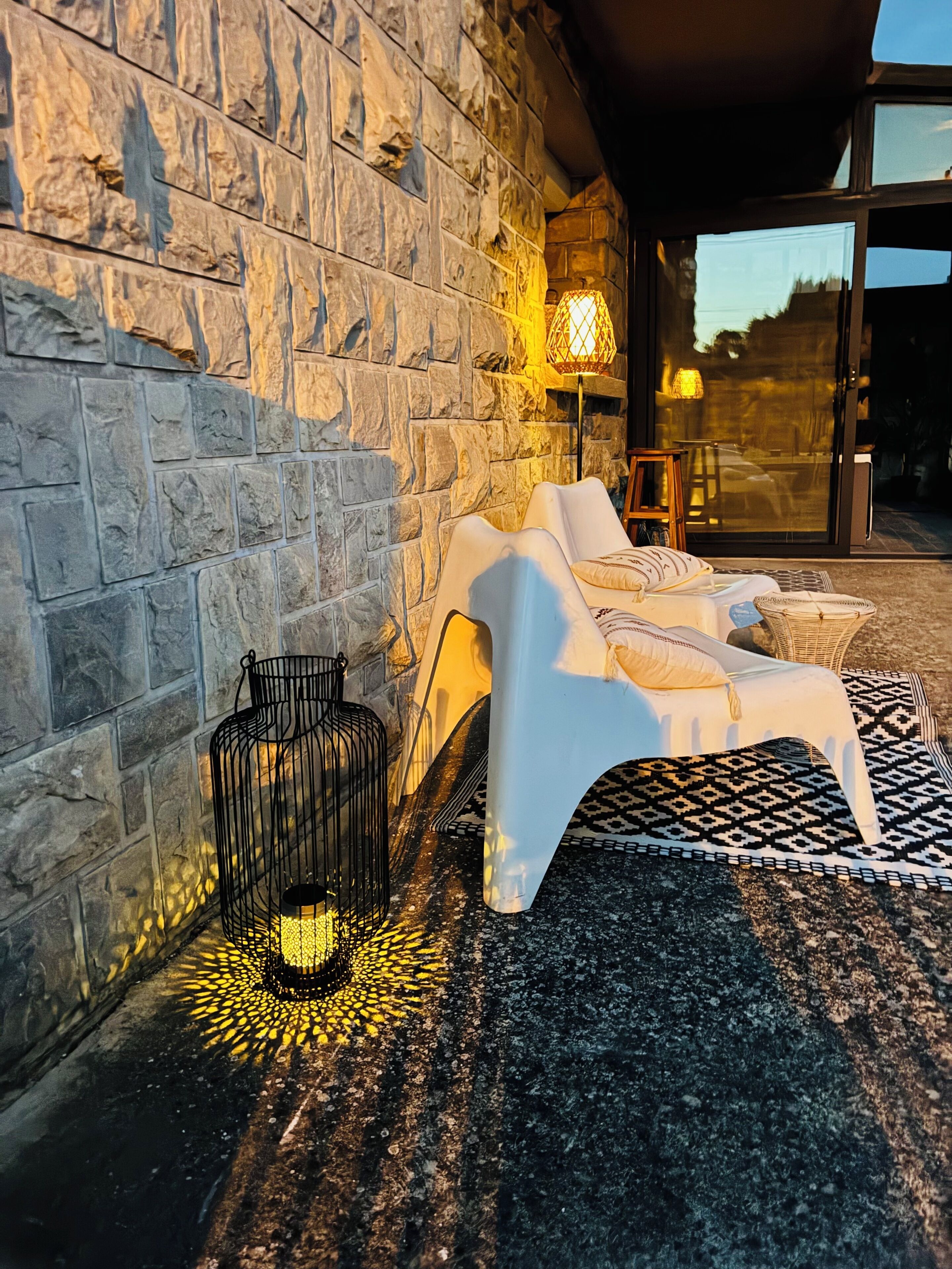 A stone wall, a white lounge chair, a wicker basket, and a floor lamp.