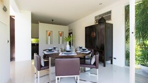 A modern dining area with a round table set for six, surrounded by chairs. - Villa Koru (Surat Thani)