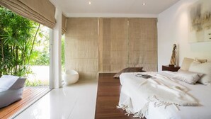A modern bedroom with a large bed, a bedside table, a lamp, and a view of greenery outside. - Villa Koru (Surat Thani)