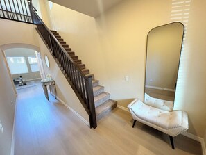 Eine Treppe mit dunkler Geländer, ein Spiegel und ein mit Stoff überzogener Sessel in einem Raum mit hellen Wänden und Holzböden.