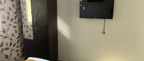 A room with a bed, a wardrobe, a television mounted on the wall, and a window with curtains.
